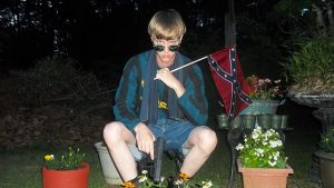 Dylann Roof staring eerily into the camera while holding a Confederate flag.